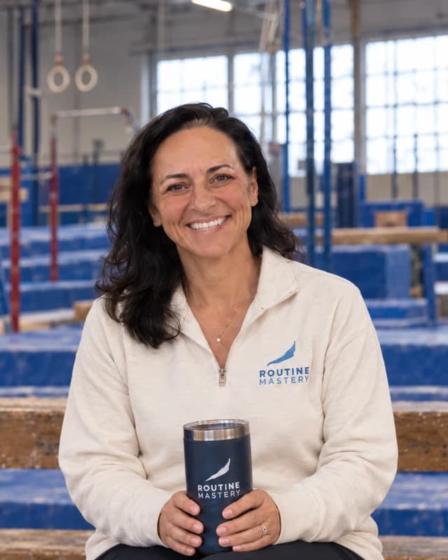 Robyn, seated on the gym bleachers holding a Routine Mastery tumbler